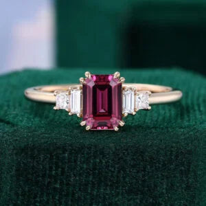Gold engagement ring with an emerald-cut raspberry garnet and baguette side stones.