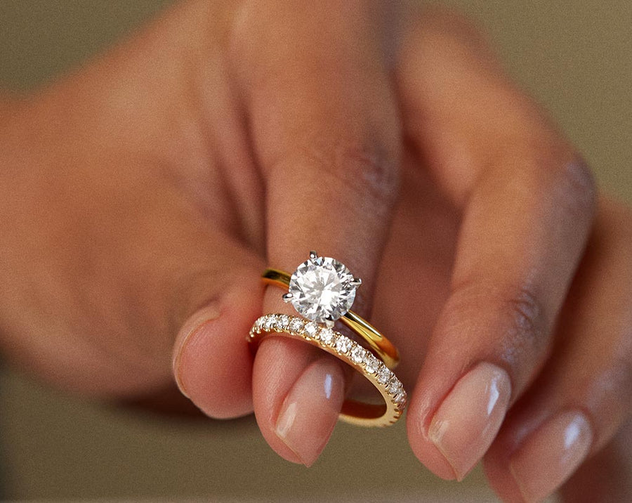 Hand holding a gold solitaire engagement ring and matching diamond wedding band.