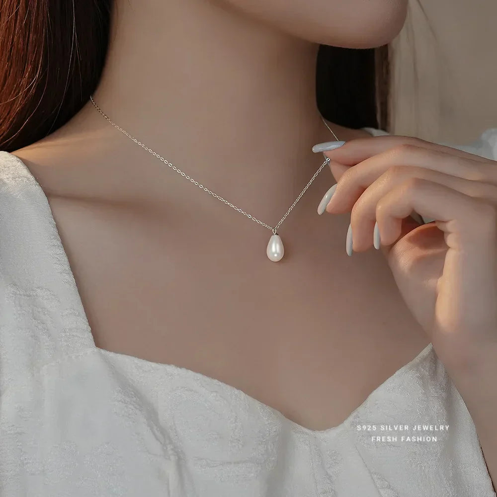 Close-up of a woman wearing a delicate silver necklace with a teardrop pearl pendant, paired with a textured white dress and long white manicured nails.