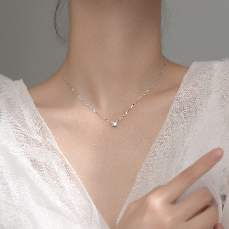 Minimalist silver necklace with a small solitaire gemstone pendant worn with a soft white tulle-style top in a close-up portrait.