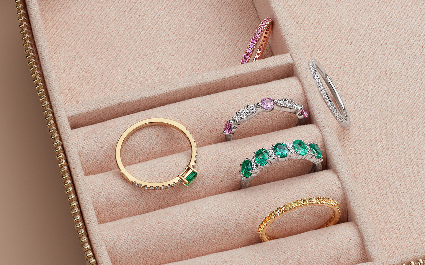 Assorted gemstone rings arranged in a blush pink jewelry case.