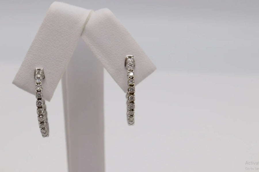 Silver hoop earrings with round clear stones displayed on a white jewelry stand.