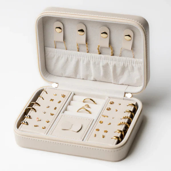Open cream jewelry travel case filled with gold earrings, rings, necklaces, and small accessories.