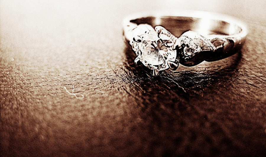 Sepia close-up of a diamond engagement ring on a textured dark surface.