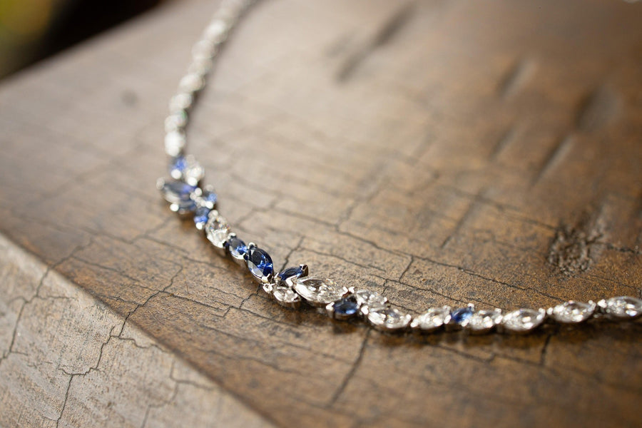 Delicate silver necklace with blue and clear gemstones resting on a rustic wooden surface.