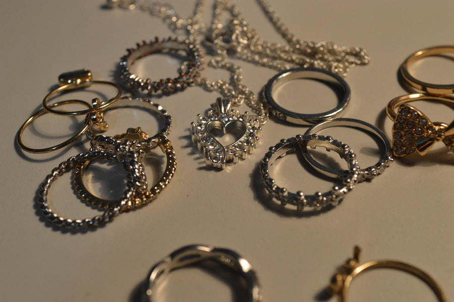 Collection of gold and silver rings and necklaces scattered on a surface under warm lighting.
