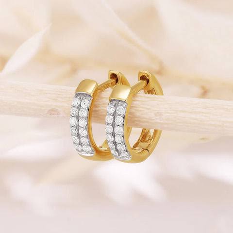 Gold hoop earrings with clear stones on a soft pink satin background.