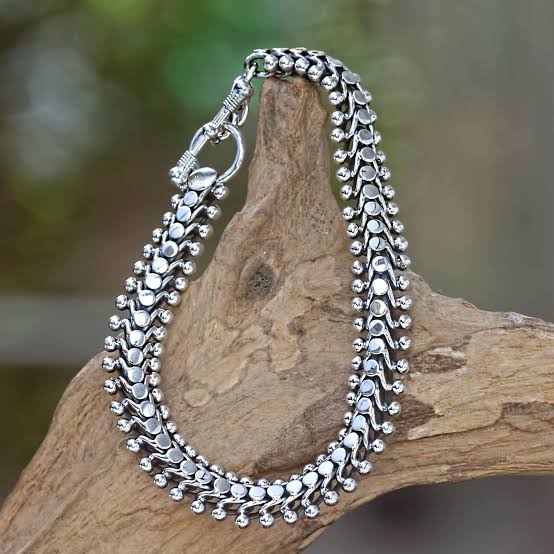 Silver statement necklace with leaf-shaped links displayed on rustic wood.
