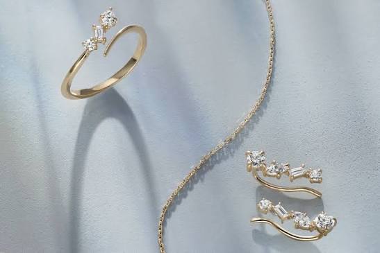 Gold ring, necklace, and matching curved earrings with clear stones on light blue fabric.