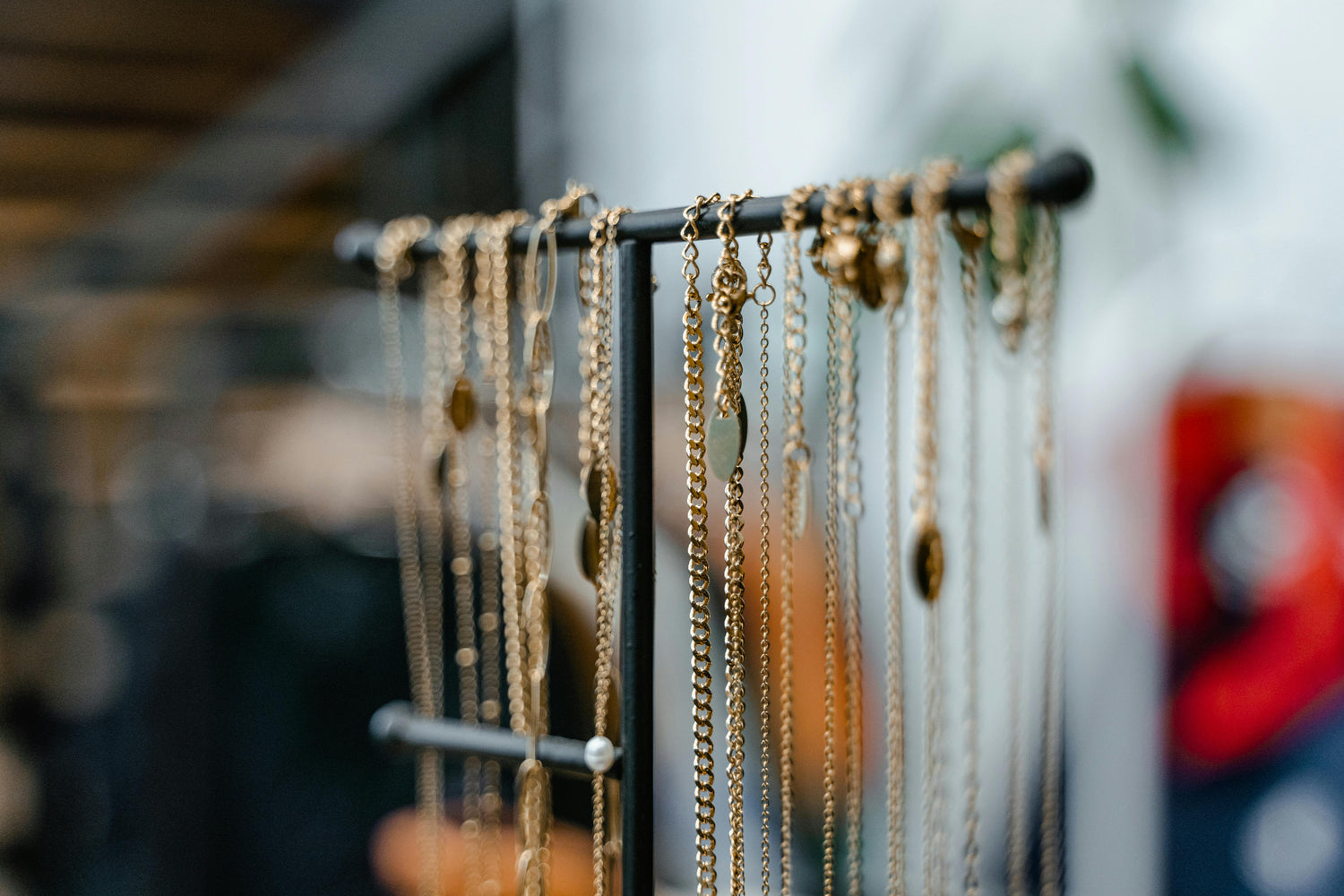 Gold necklaces hanging on a black jewelry stand with a softly blurred indoor background.