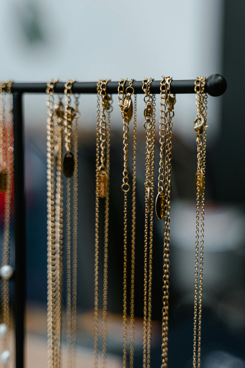 Gold chain necklaces hanging from a black jewelry display stand with a blurred background and soft lighting.