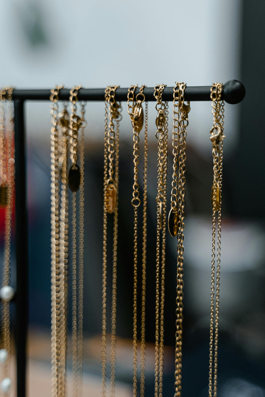 Gold chain necklaces hanging from a black jewelry display stand with a blurred background and soft lighting.