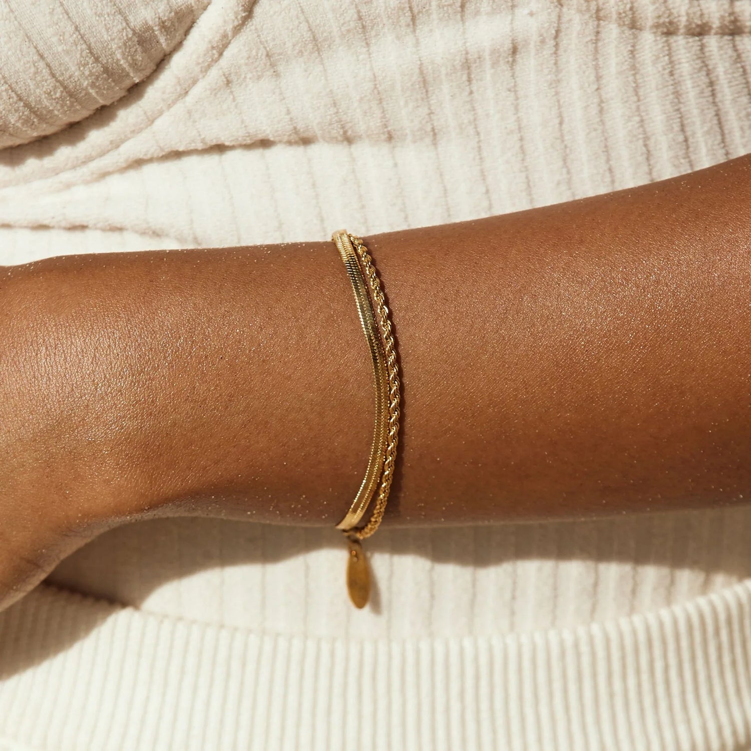 Two layered gold chain bracelets worn on a wrist.