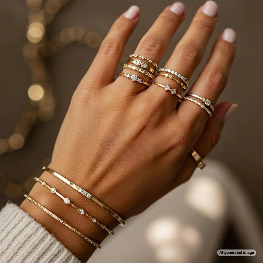 Hand wearing stacked gold rings and bracelets accented with clear stones.